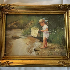 May include: A framed painting depicts a young child with a butterfly net standing near a stream. The child is wearing a white outfit and a blue bow. The painting is in a gold ornate frame.