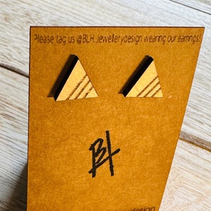 May include: A pair of wooden triangle earrings with a striped pattern. The earrings are displayed on a brown card with the text "Please tag us @BLH.Jewellerydesign wearing our earrings!" and the initials "BL" in black.