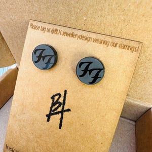 May include: A pair of black wooden earrings with a silver 'FF' logo. The earrings are displayed on a brown card with the text 'Please tag us @BLH. Jewellerydesign wearing our earrings!' and 'Instagram: blh.jewellen'.