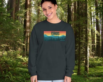 Op de afbeelding: Een donkergroen longsleeve shirt met een retro-grafische afbeelding van een bergketen en de tekst "Save the Forest We Need You" in een kleurrijk banner.
