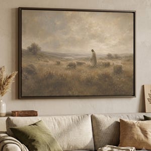 May include: A rectangular framed wall art print depicting a pastoral landscape in muted earth tones. The scene features a figure in a long robe walking through a grassy field among a flock of sheep under a cloudy, overcast sky.