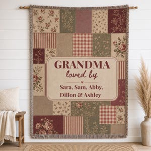 May include: A rectangular woven throw blanket featuring a patchwork design of floral, striped, and checkered patterns in muted red, green, and beige tones. The center displays the text "GRANDMA loved by" followed by the names "Sara, Sam, Abby, Dillon & Ashley".