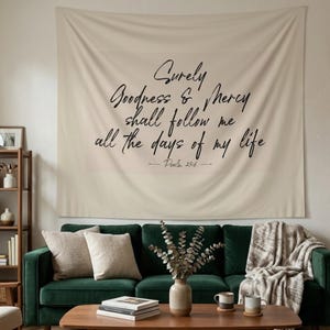 May include: A rectangular beige wall tapestry featuring the black printed text: Surely Goodness & Mercy shall follow me all the days of my life — Psalm 23:6. The fabric is draped flat against the wall, displaying a clean, minimalist aesthetic.