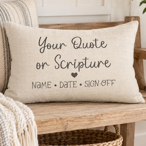 May include: A rectangular beige linen throw pillow featuring dark gray printed text that reads Your Quote or Scripture, followed by a small heart icon and the words NAME • DATE • SIGN-OFF centered on the front of the fabric cover.