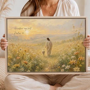 May include: A rectangular framed wall art print featuring a painting of a figure in a robe walking with a small lamb through a field of yellow and white wildflowers at sunset. The text "He restores my soul Psalms 23:3" is printed in the upper left corner.