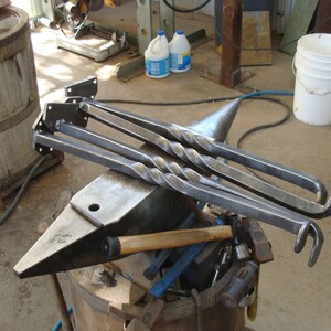 May include: Four metal legs with a twisted design are resting on an anvil. The legs are made of steel and have a black finish. The anvil is made of metal and has a grey finish.