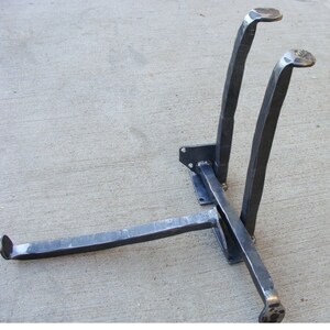 May include: A metal stand with three legs, two of which are curved and one straight. The stand is made of black metal and has a rustic, industrial look.