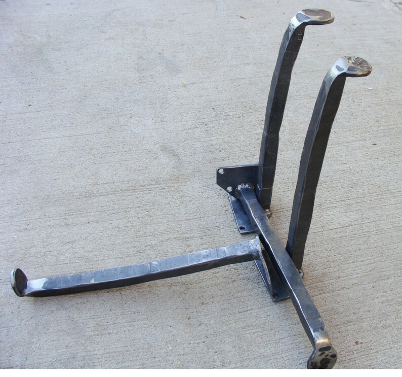 May include: A metal stand with three legs, two of which are curved and one straight. The stand is made of black metal and has a rustic, industrial look.
