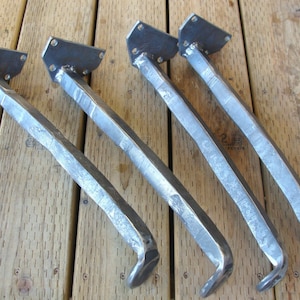 May include: Four metal table legs with a square base and a curved design. The legs are made of hammered metal and have a silver finish.