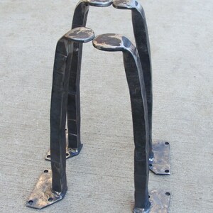 May include: Three black metal hairpin legs with a hammered finish. The legs are designed to be attached to a table or other furniture piece.