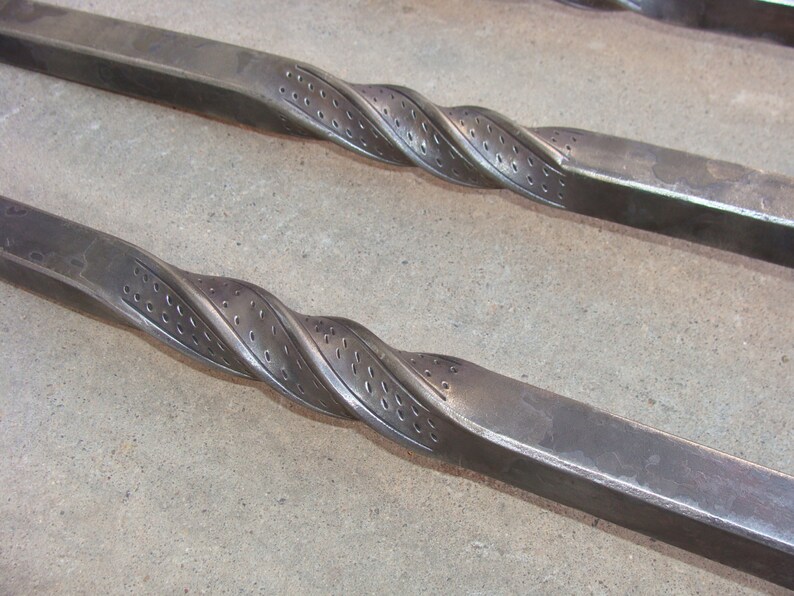 May include: Two long, twisted metal rods with a decorative pattern of holes. The rods are made of a dark metal and have a rough, textured surface.