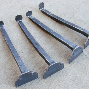 May include: Four metal table legs with a rounded top and a flat, triangular base. The legs are made of dark metal and have a hammered finish.