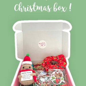 May include: A pink Christmas gift box with the text "Positive potato Christmas box!" contains a crocheted potato figure wearing a Santa hat, a red scrunchie, a bracelet, and a sticker.