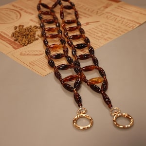 Puede incluir: Un collar de cuentas marrones y ámbar con dos cierres dorados. El collar está hecho de cuentas ovaladas y está enhebrado en un patrón.