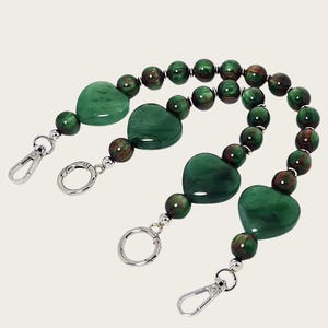 May include: Two beaded purse straps with heart-shaped and round green beads, interspersed with brown and green beads. The straps have silver-colored clasps and rings for attachment.