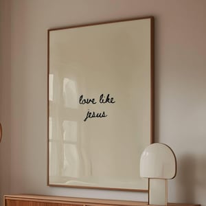Puede incluir: Un salón con un sofá blanco curvado, una mesa de centro de madera con tapa de cristal y un aparador de madera. Un gran cuadro enmarcado con el texto "love like jesus" cuelga sobre el aparador. También se ven una lámpara moderna y una lámpara de pie circular.