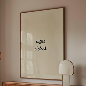 May include: A modern living room with a cream-colored sofa, a wooden coffee table with a glass top, and a wooden cabinet. A large framed print with the words "coffee o'clock" hangs on the wall. A white lamp sits on the cabinet.