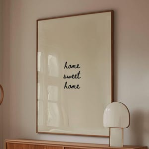 May include: A cozy living room scene featuring a white, curved sofa, a wooden coffee table with a glass top, and a wooden cabinet. A large framed print with the words "home sweet home" hangs above the cabinet. A white lamp and a wooden floor lamp are also visible.