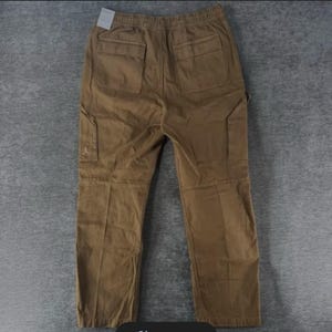 May include: Brown cargo pants with multiple pockets, including two back pockets and two side pockets. The pants have an elastic waistband and a small logo on the side pocket. The pants are made of a durable material and are suitable for casual wear.