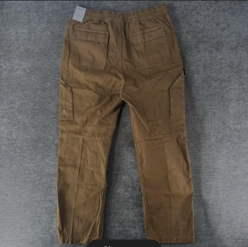 May include: Brown cargo pants with multiple pockets, including two back pockets and two side pockets. The pants have an elastic waistband and a small logo on the side pocket. The pants are made of a durable material and are suitable for casual wear.