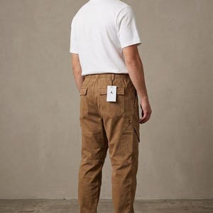 May include: A person wearing a white t-shirt and brown cargo pants. The pants have multiple pockets and a tag. The person is also wearing brown and white sneakers. The outfit is casual and stylish.