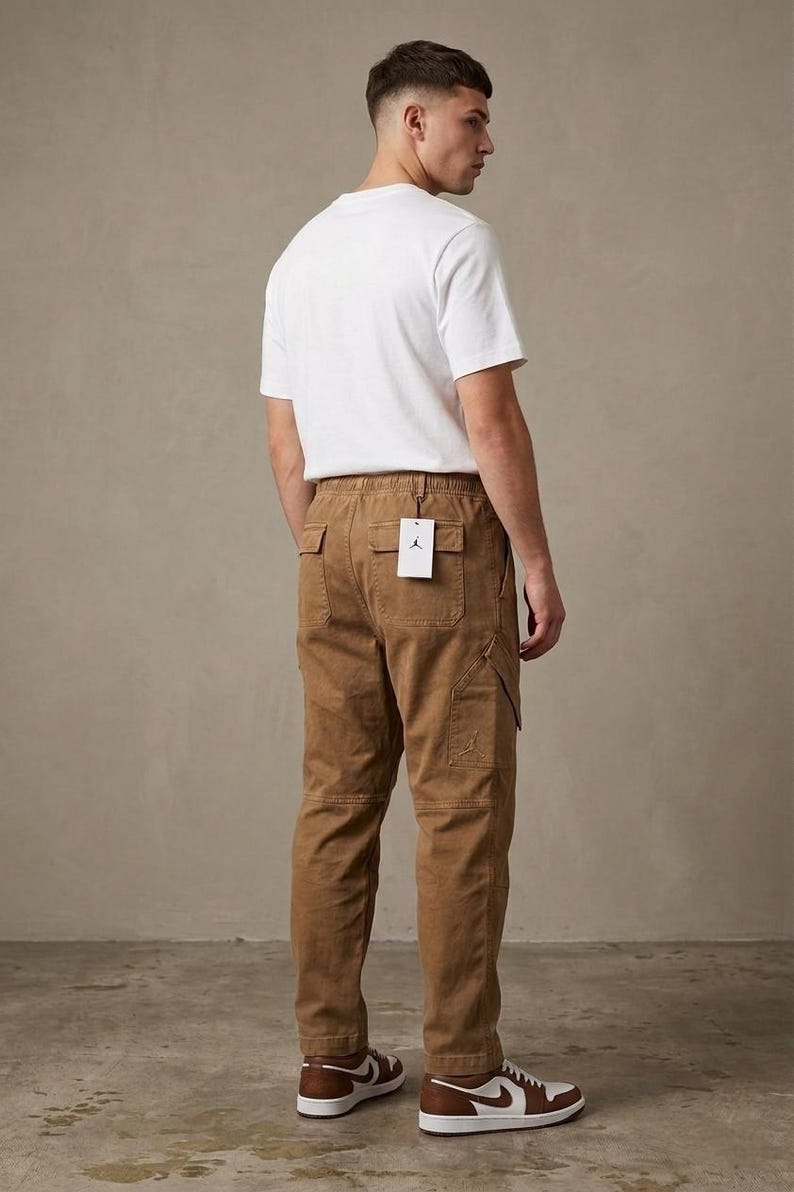 May include: A person wearing a white t-shirt and brown cargo pants. The pants have multiple pockets and a tag. The person is also wearing brown and white sneakers. The outfit is casual and stylish.