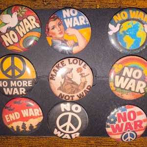 May include: A collection of nine round pinback buttons with anti-war messages. The buttons feature images of doves, rainbows, peace signs, and the text "NO WAR," "NO MORE WAR," and "END WAR!" in various colors.