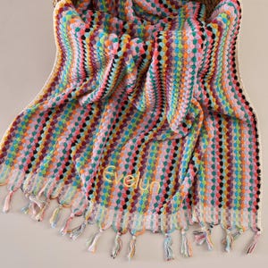 以下が含まれることがあります： フリンジの縁取りと黄色い糸で刺繍された「Evelyn」という名前がついた、カラフルなストライプのタオルです。
