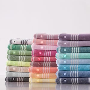 Puede incluir: Una colección de toallas turcas plegadas en varios colores, incluyendo blanco, verde, rosa, rojo, naranja, amarillo, azul y morado. Cada toalla presenta un diseño a rayas. Las toallas están apiladas en montones ordenados, mostrando una gama de tonos.