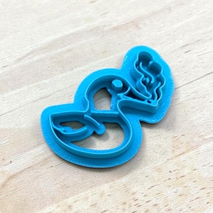 May include: A bright blue plastic cookie cutter in the shape of a pelican. The pelican has a long beak and a pouch. The cutter is on a light wood surface.