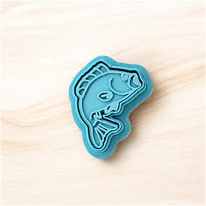 Könnte beinhalten: Blauer Plastik-Ausstecher in Form eines Fisches. Der Fisch ist nach rechts gerichtet und hat ein detailliertes Design.