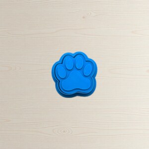 May include: A bright blue paw print cookie cutter. The cutter has a three-dimensional design with a detailed paw shape, perfect for creating pet-themed treats. The cutter is made of plastic.
