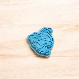 May include: A blue plastic cookie cutter shaped like a cartoon bee. The bee has large eyes and wings.