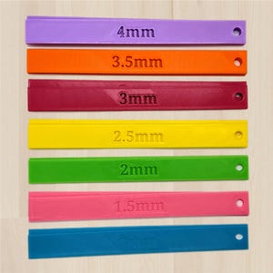 May include: Seven brightly coloured plastic measuring tools. Each tool is a different colour, including purple, orange, and green, and has a measurement in millimetres, ranging from 1mm to 4mm. Each has a hole at one end.