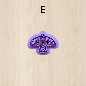 Puede incluir: Un cortador de galletas morado con forma de p&aacute;jaro con intrincados dise&ntilde;os de hojas y corazones. El cortador de galletas tiene una parte superior redondeada y un contorno detallado, perfecto para crear galletas decorativas. La letra "E" est&aacute; en el centro superior.