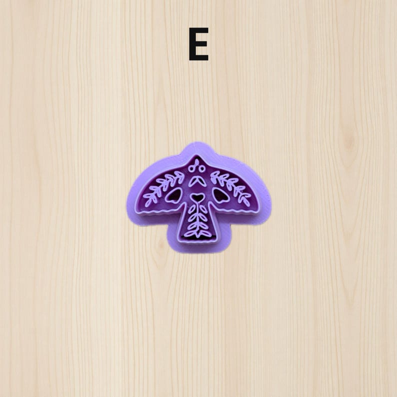 Puede incluir: Un cortador de galletas morado con forma de p&aacute;jaro con intrincados dise&ntilde;os de hojas y corazones. El cortador de galletas tiene una parte superior redondeada y un contorno detallado, perfecto para crear galletas decorativas. La letra "E" est&aacute; en el centro superior.