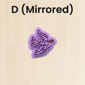 Puede incluir: Un cortador de galletas morado con forma de p&aacute;jaro con intrincados patrones florales y de hojas. El cortador tiene un dise&ntilde;o de espejo y est&aacute; sobre un fondo de madera clara. El texto "D (Mirrored)" est&aacute; en la parte superior.