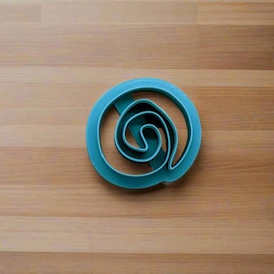 May include: Teal plastic cookie cutter shaped like a spiral with three concentric circles.
