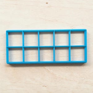 May include: A bright blue plastic cookie cutter featuring a rectangular frame divided into ten equal square compartments arranged in two rows of five. The tool has a flat, open design with thin walls, creating a grid pattern for cutting dough.
