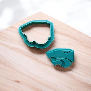 May include: Two teal blue plastic cookie cutters, one shaped like a paw print and the other shaped like a head of a lion.