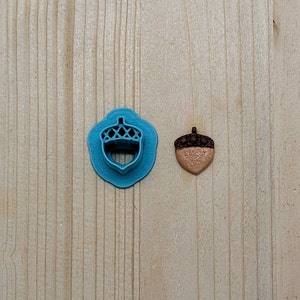 May include: A blue plastic acorn-shaped cookie cutter and a brown acorn-shaped cookie.