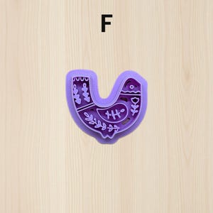 Puede incluir: Un cortador de galletas morado con forma de p&aacute;jaro, con patrones florales y geom&eacute;tricos decorativos. La letra "F" est&aacute; encima del cortador de galletas. El dise&ntilde;o del p&aacute;jaro incluye un ojo peque&ntilde;o, un pico y una cola.