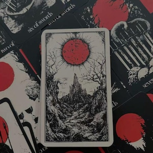 May include: A deck of tarot cards with a gothic aesthetic. The central card features a black and white illustration of a landscape with a red sun. Other cards show similar imagery, including a red circle and various symbols.