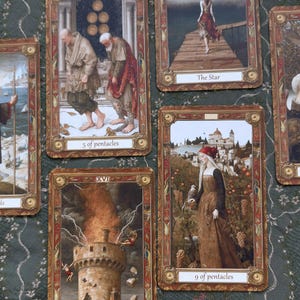 Może przedstawiać: Kolekcja pięciu prostokątnych kart tarota ze szczegółowymi ilustracjami. Karty obejmują The Star, 5 of Pentacles, 9 of Pentacles oraz The Tower, każda z ozdobnymi złotymi obramowaniami i opisowymi etykietami tekstowymi na dole.