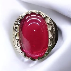 May include: A silver ring featuring a large, oval-shaped, red gemstone set in an ornate, decorative setting.