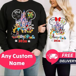 May include: Black sweatshirt with a Disney design featuring Mickey and Minnie Mouse, a castle, and the text "Disney Paris 2026". A white hoodie with a similar design is also shown. The design is in the shape of Mickey Mouse's head.