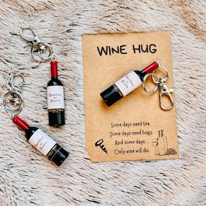 May include: Miniature wine bottle keychains with red and black details, attached to silver keyrings. The label reads "Casillero del Diablo". A card with the text "WINE HUG" and a wine-related quote is also present.