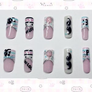 Könnte beinhalten: Ein Set aus zehn künstlichen Nägeln mit verschiedenen Designs. Die Nägel haben eine rosa Basis mit weißen, blauen und silbernen Akzenten. Einige Nägel haben Text, darunter "#bff", "#lol" und "3". Andere haben Cartoon-Designs.