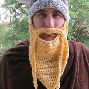 May include: A crocheted Viking hat with horns and a matching beard. The hat is gray and the beard is yellow.