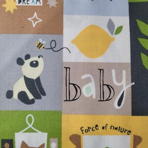 May include: A colorful fabric with a patchwork design featuring various illustrations and text. The design includes a panda, a lemon, a frog, a fox, and the word "DREAM" and "BABY". The color palette includes brown, green, yellow, and gray.